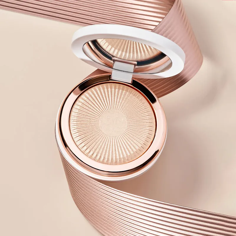 Aerial view of a closed compact highlighter with a textured, radiant design on a beige and pink background.