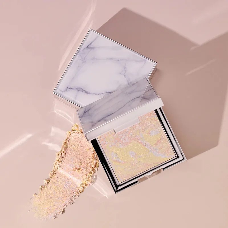 Open compact with marble lid and swatch of shimmery powder on a beige surface.