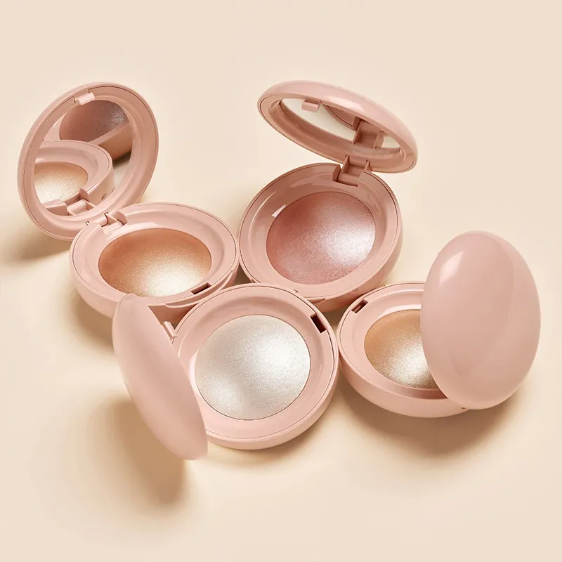 Four open round makeup compacts with various shades of highlighter on a beige background.