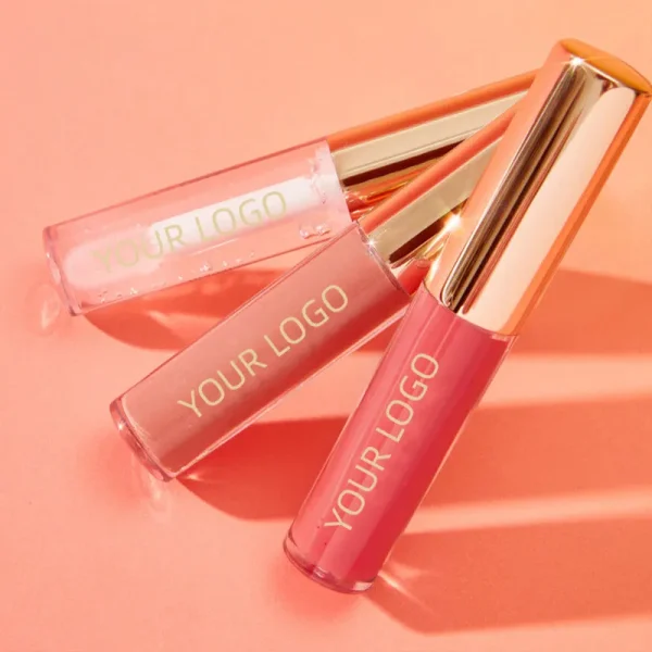 Three lip gloss tubes with gold caps lying on a pink surface.