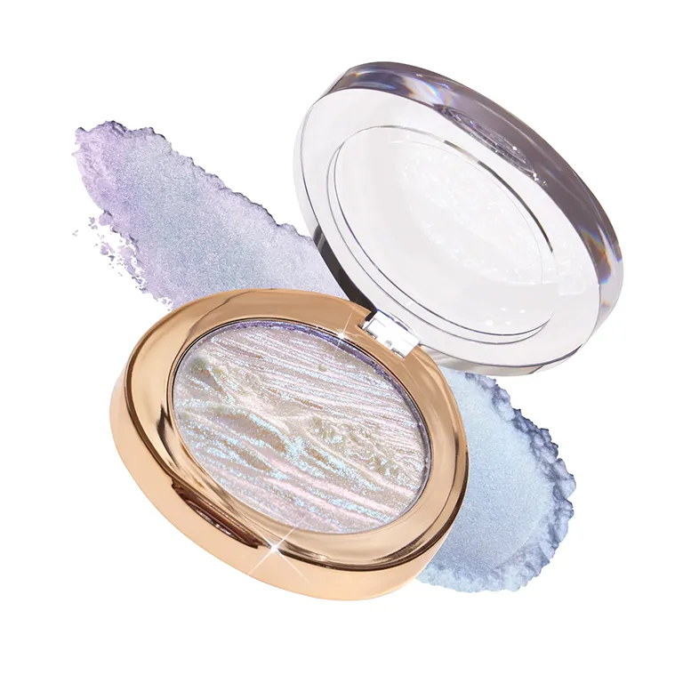 A compact opened to reveal a shimmering highlighter with a blue and purple swirled texture. The compact has a golden rim and is placed over smudged highlighter powder.