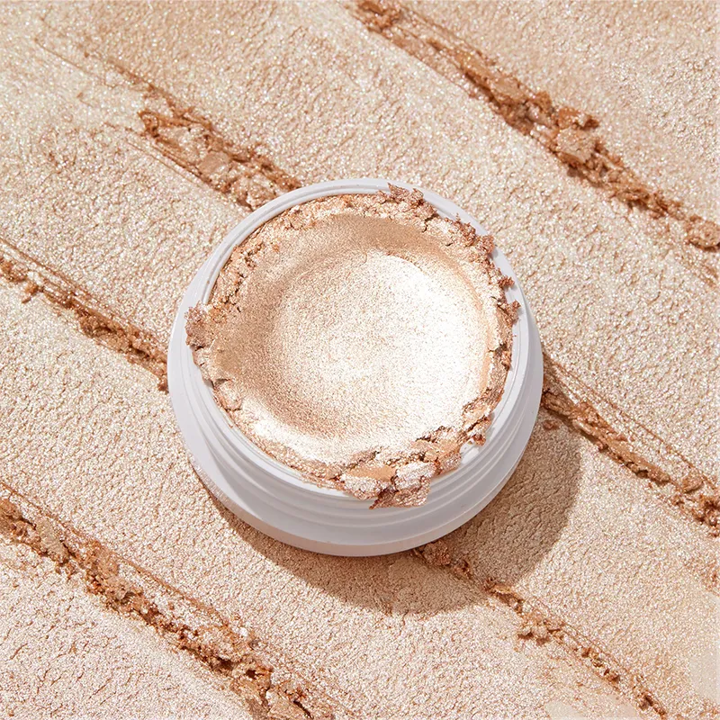 Open jar of shimmery gold makeup on textured background