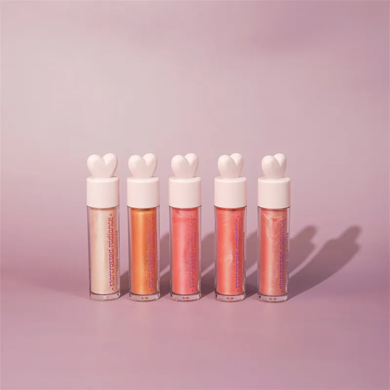 Five tubes of Starcrossed Radiance liquid highlighter with heart-shaped caps in various shades against a pink background.