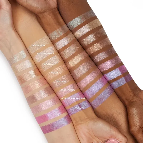 Four arms of varying skin tones lined up with different shimmery and matte makeup swatches labeled with names like 'SAGE BUNDLE', 'FIELD OF FAIRIES', 'MYSTICAL', 'BUZZY', 'BOO-KAY', 'CLOSE TO YOU', 'NO REST FOR THE VIVID', and 'DUCKLING'.
