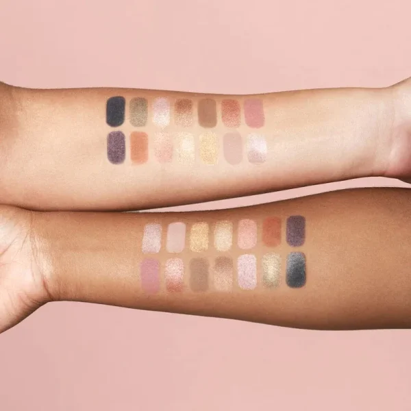 Two arms displaying swatches of neutral eyeshadow shades on a light pink background.