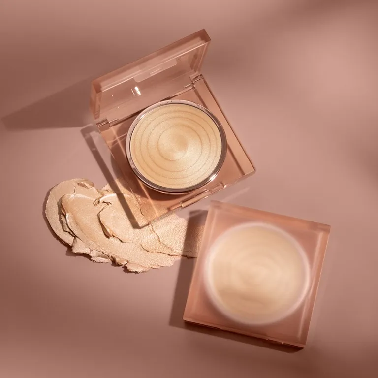 Open compact of Becca highlighter with streak of product on pink background.