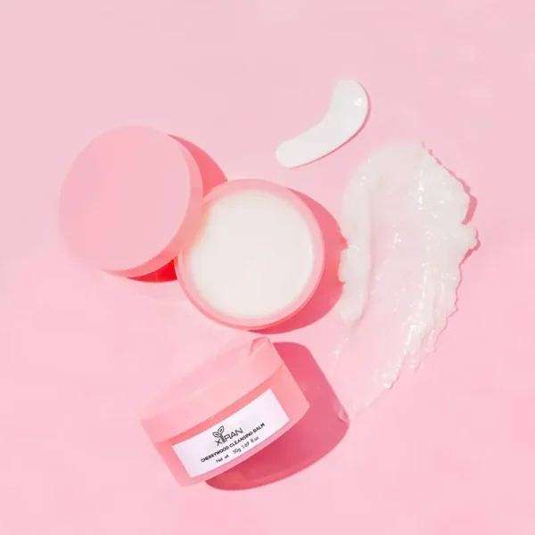 Open jar of cleaning balm on a pink background with some balm smeared beside it.
