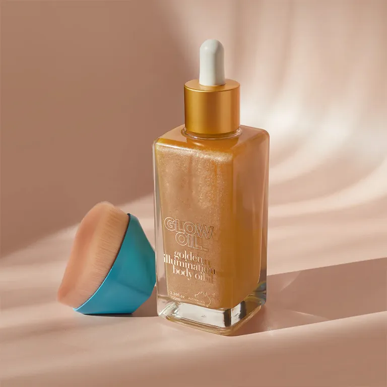 A bottle of Glow Oil golden illumination body oil with an applicator brush.