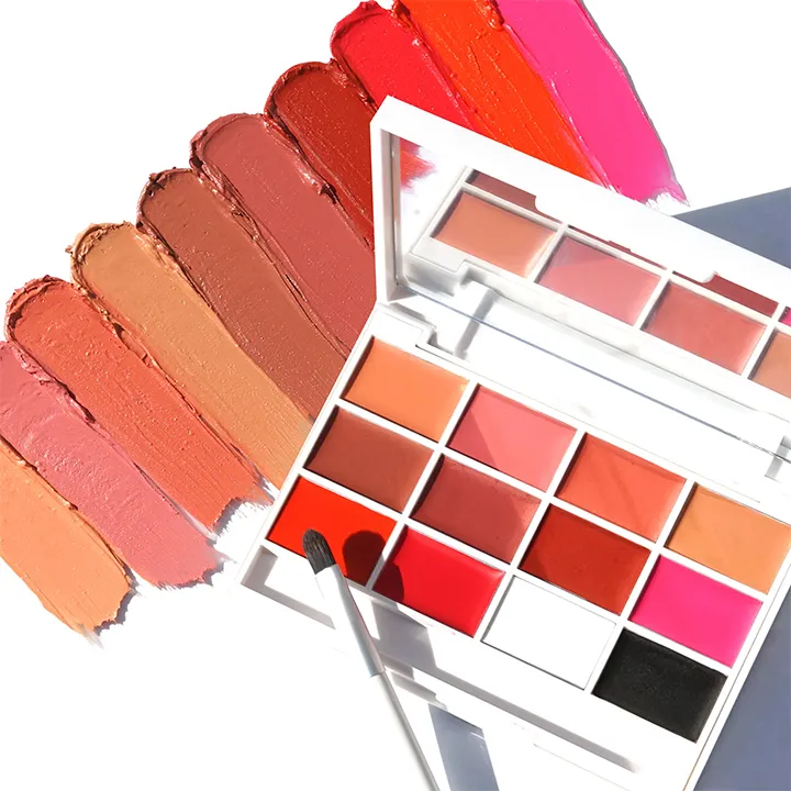 A white lipstick palette with various shades of red, orange, pink, and black with a brush, displayed on a white surface.