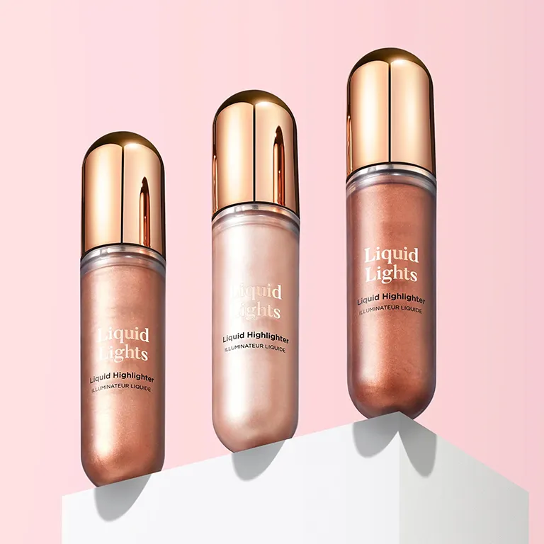 Three bottles of Liquid Lights highlighter in different shades on a white platform against a pink background.