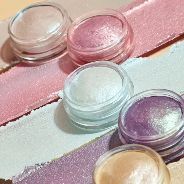 A selection of metallic eyeshadow in small jars with strips of color on a surface