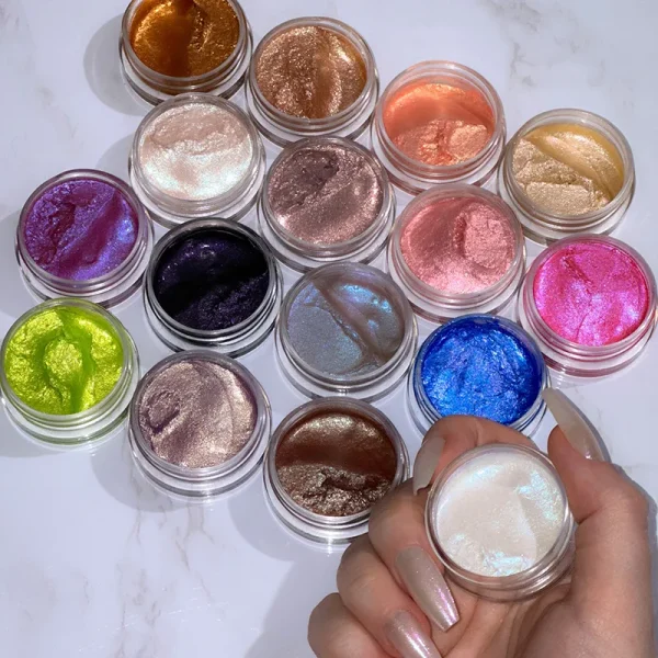 A collection of round containers filled with various colorful shimmering gels arranged on a white surface, featuring colors like gold, copper, pink, blue, and purple with a hand holding a white shimmering gel.