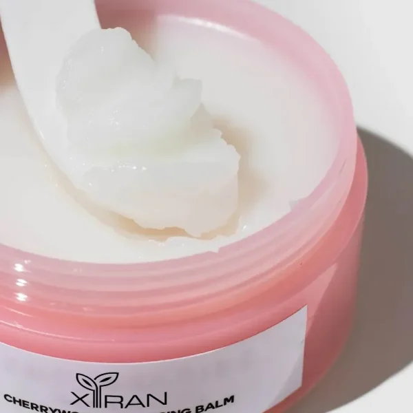 A pink container of Xiran Cherry Blossom Cleansing Balm with a scoop of balm on a spatula.