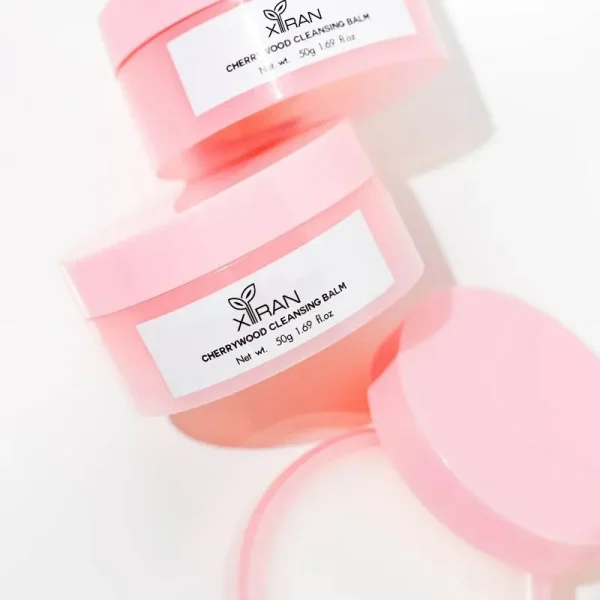 Two pink jars of Xiran Cherrywood Cleansing Balm with lids slightly open.