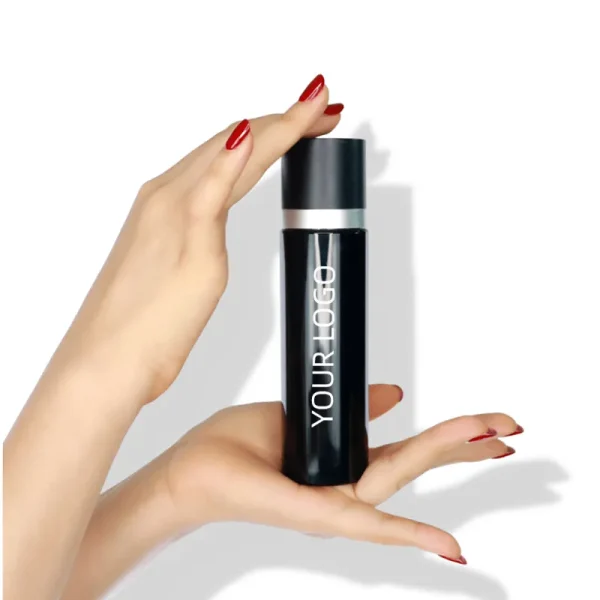 A person's hand holding a black cylindrical cosmetic bottle labeled 'YOUR LOGO' with a silver cap, showcasing a potential branding design.