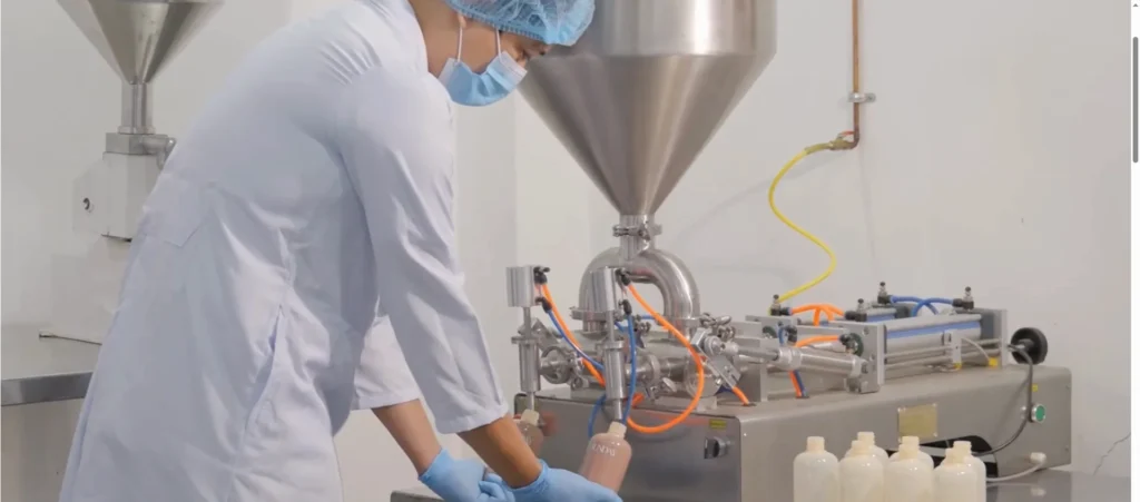 Person in lab coat and gloves operates a bottle filling machine dispensing liquid into containers.