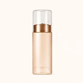 A sleek cylindrical beauty product bottle with a gold base and a transparent cap on a neutral background.