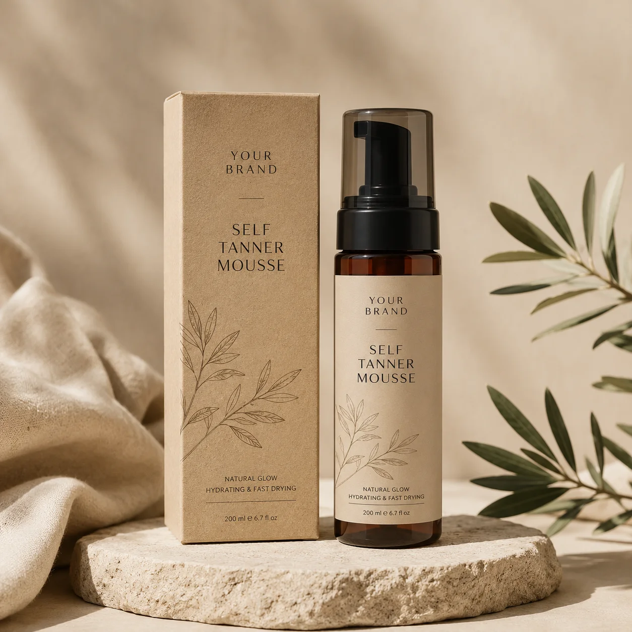 A bottle of self tanner mousse with a matching box, displayed on a natural stone surface with beige fabric and green leaves.